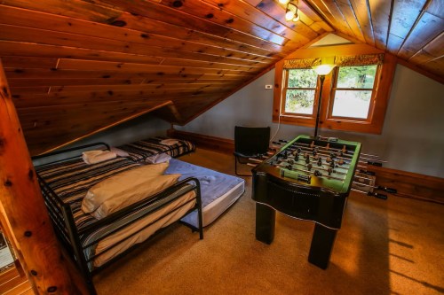 Cozy attic room with a bed, a chair, and a foosball table under a wooden ceiling.