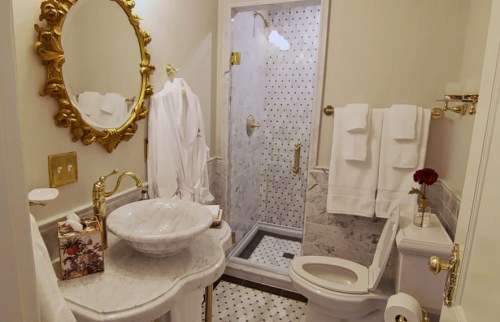 Elegant bathroom featuring a marble sink, gold accents, a shower, and plush white towels.