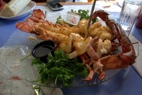 A seafood platter featuring grilled lobster and shrimp, garnished with parsley and served with a dipping sauce.