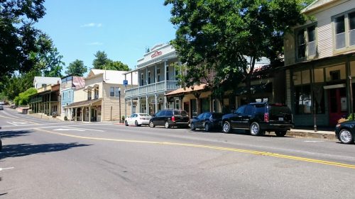 A quiet street lined with historic buildings and parked cars under a clear blue sky.
