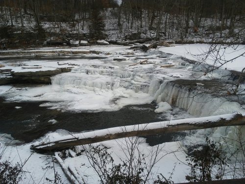 A frozen waterfall surrounded by snow-covered rocks and trees in a winter landscape.