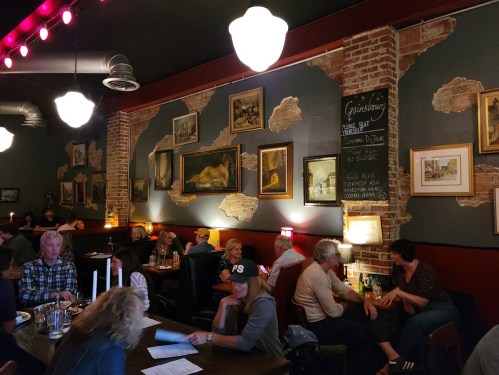 A cozy restaurant interior with exposed brick walls, artwork, and diners enjoying their meals at tables.