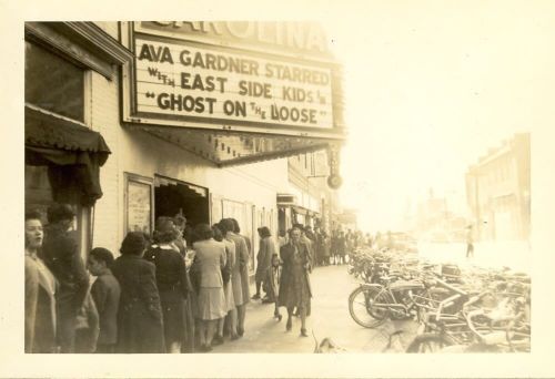 A vintage photo of a theater marquee featuring Ava Gardner, with a line of people and bicycles outside.