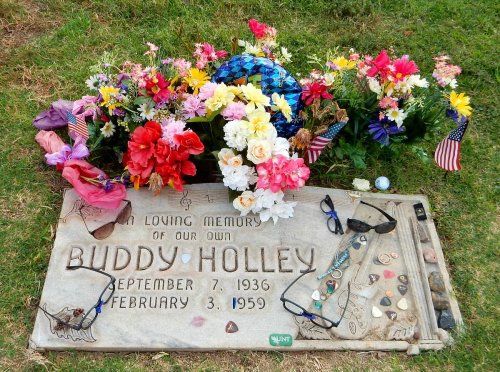 Grave of Buddy Holly, adorned with colorful flowers, sunglasses, and mementos, honoring his memory.