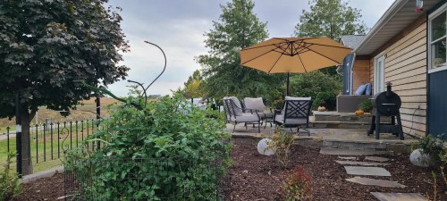 A cozy outdoor patio with an umbrella, chairs, and a garden, surrounded by trees and a scenic view.