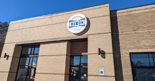 Exterior of a building featuring a sign that reads "BAKON," with a clear blue sky in the background.