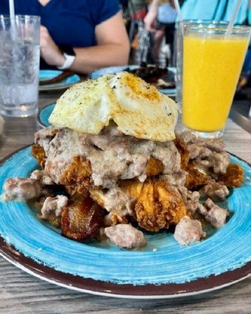 A plate of fried chicken topped with gravy and a fried egg, served with a side of orange juice.