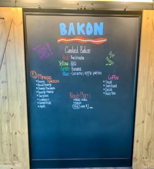 Chalkboard menu listing flavors of candied bacon and drink options like mimosas, coffee, and Bloody Marys.