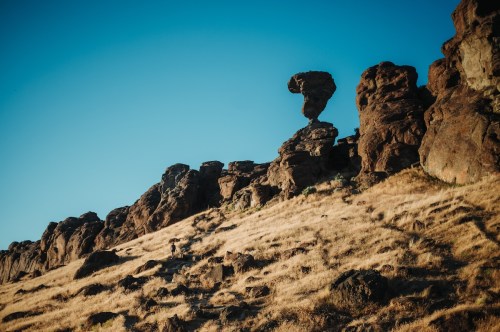 A person walking on a hillside with unique rock formations against a clear blue sky.
