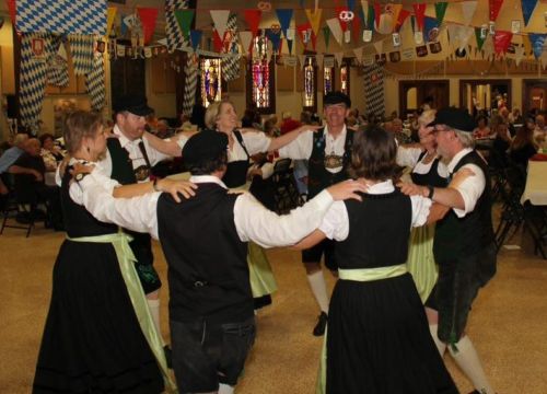 A group of dancers in traditional attire performing in a festive hall decorated with colorful banners.