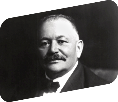 Black and white portrait of a man with a mustache, wearing a suit and bow tie, looking directly at the camera.