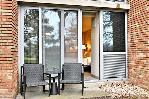 Two wicker chairs and a small table on a patio, with a view of a room through sliding glass doors.