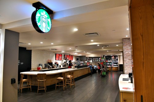 Interior of a Starbucks with a counter, seating, and a green logo sign, featuring a modern design and warm lighting.