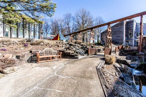 A serene garden path with a wooden bench, stone features, and a small stream under a clear blue sky.