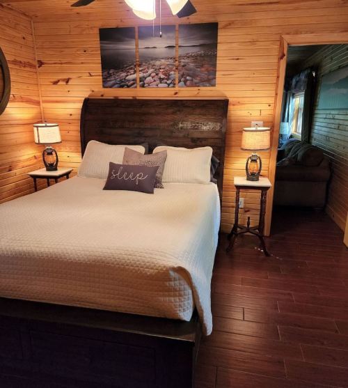 Cozy bedroom with a wooden bed, white bedding, and decorative pillows, featuring warm wood paneling and soft lighting.