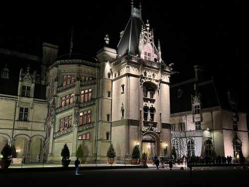 A grand mansion illuminated at night, showcasing intricate architecture and a welcoming entrance.