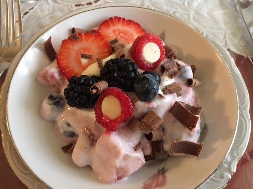 A dessert bowl filled with yogurt, mixed berries, and chocolate shavings, garnished with sliced strawberries and raspberries.