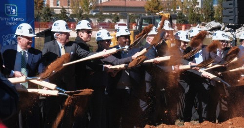 Group of people in hard hats using shovels to break ground at a construction site for Fifth Third Bank.