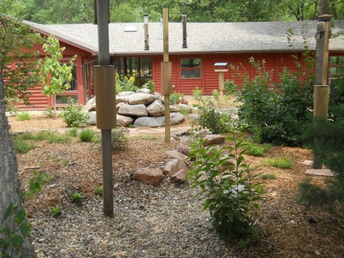 A landscaped garden with rocks, plants, and birdhouses, set against a red building in a natural setting.