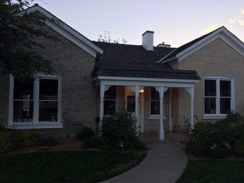 A charming two-story house with a front porch, surrounded by greenery and a well-maintained lawn at dusk.