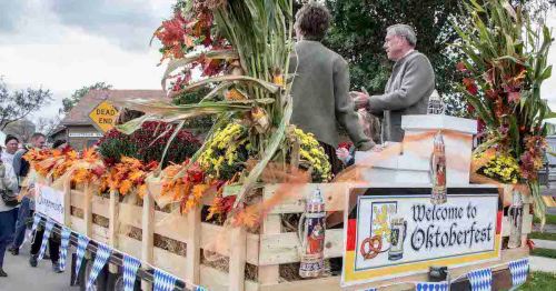 A festive parade float decorated with autumn leaves and flowers, welcoming attendees to Oktoberfest.