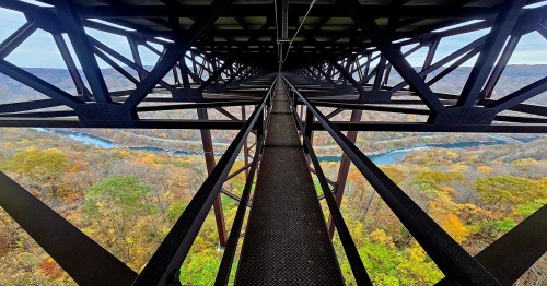 View from a metal bridge structure, overlooking a river and colorful autumn foliage below.