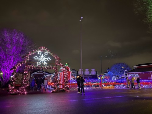 Colorful holiday lights illuminate a festive scene with a snowflake arch and people enjoying the decorations at night.