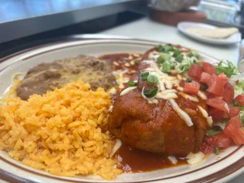 A plate of enchiladas topped with sauce, cheese, lettuce, and tomatoes, served with rice and refried beans.