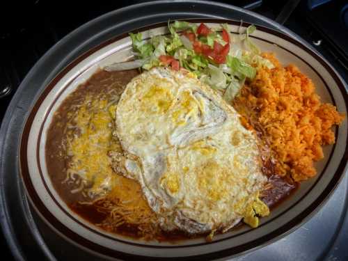 A plate of rice, beans, and two fried eggs topped with cheese, served with lettuce and tomato on the side.