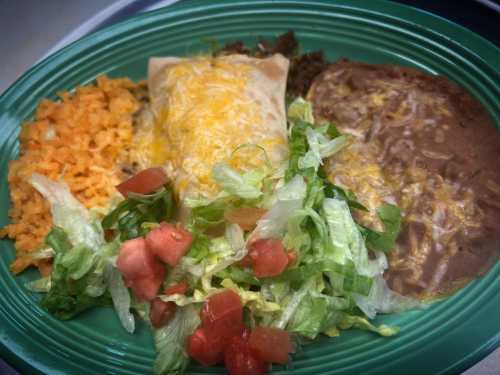 A green plate with a burrito topped with cheese, rice, refried beans, and a fresh salad of lettuce and tomatoes.