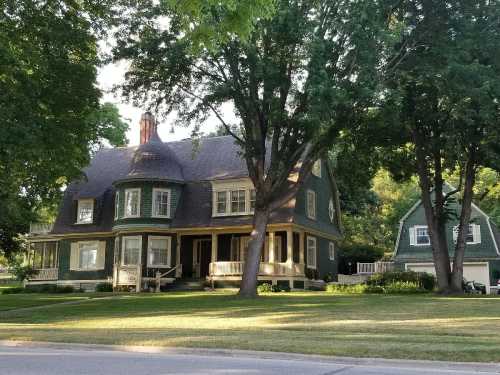 A large green Victorian-style house with a wraparound porch, surrounded by trees and a well-maintained lawn.