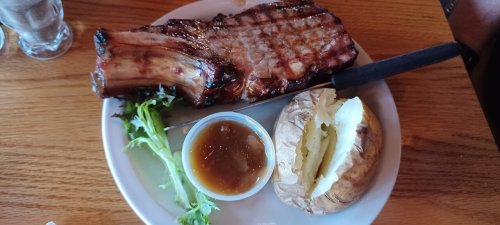 A grilled ribeye steak with a baked potato and gravy on a plate, garnished with lettuce.