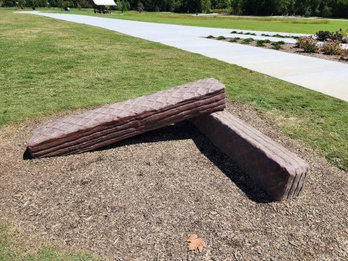 Two large, textured stone benches positioned at an angle on grassy ground in a park setting.