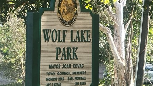 Sign for Wolf Lake Park in Florida, listing the mayor and town council members. Surrounded by greenery.