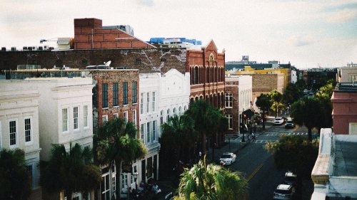 Aerial view of a charming street lined with historic buildings and palm trees under a bright sky.