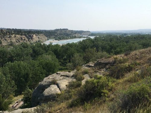 A scenic view of a river winding through lush greenery and rocky terrain under a clear sky.
