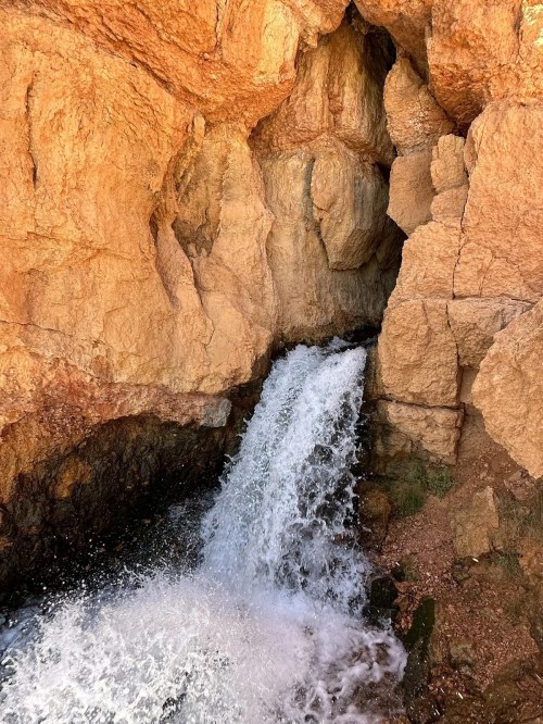 A waterfall cascading over rocky terrain, surrounded by rugged, orange-hued cliffs.