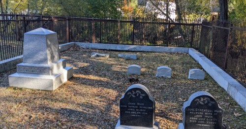 Graveyard with several headstones, including those of John Muir and his wife, surrounded by a metal fence.
