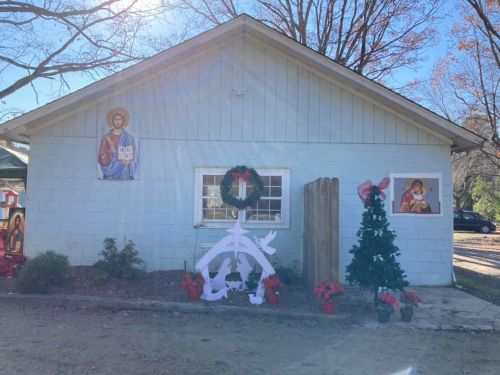 A light blue building decorated for the holidays, featuring religious images, a wreath, and festive plants.