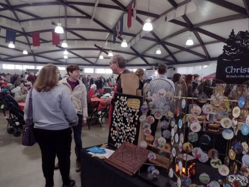 A busy indoor market with vendors and shoppers, featuring crafts and decorations, under a high ceiling with flags.