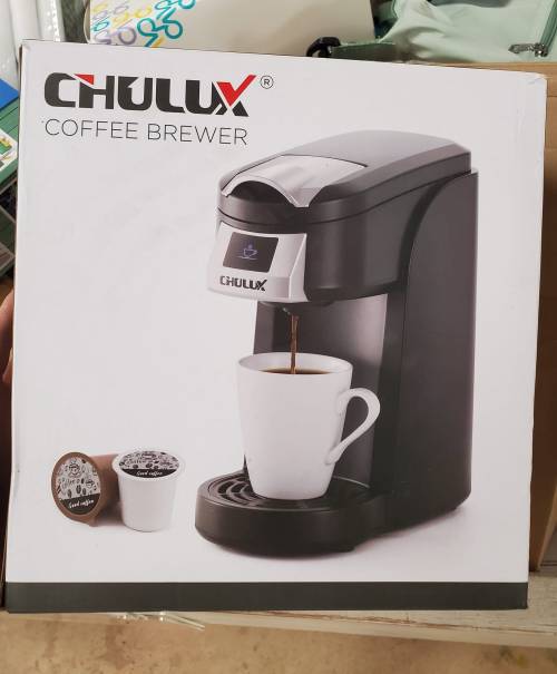 A coffee brewer with a white mug and coffee pod, displayed on its packaging.