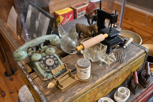 A collection of vintage items including a rotary phone, glass figurines, and a small press on a colorful table.