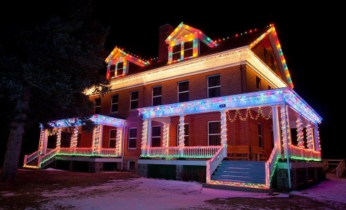 A beautifully decorated historic building illuminated with colorful holiday lights at night. Snow covers the ground.