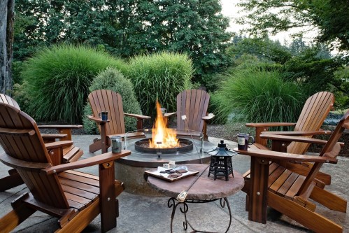 A cozy outdoor fire pit surrounded by wooden chairs and greenery, perfect for gatherings and relaxation.