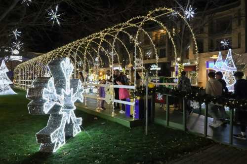 A festive night scene with illuminated decorations, people walking through a lighted archway, and snowflake displays.