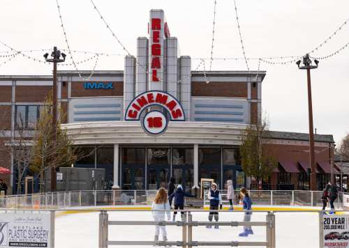 A skating rink in front of a Regal Cinemas building, with people ice skating and festive lights overhead.
