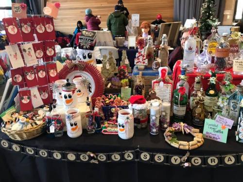 A festive market display featuring handmade crafts, holiday decorations, and colorful gift items on a table.