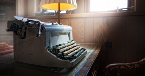 A vintage typewriter sits on a polished desk, illuminated by soft light from a nearby lamp.
