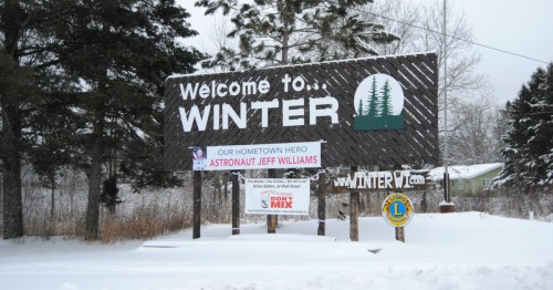 Sign welcoming visitors to Winter, featuring a tribute to astronaut Jeff Williams and snowy surroundings.