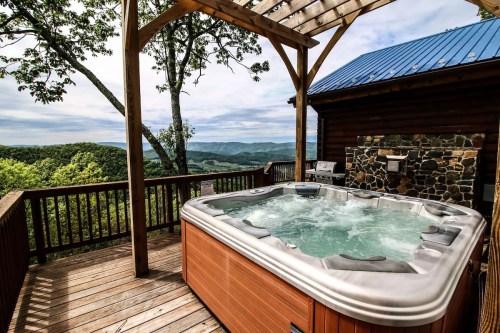 A hot tub on a wooden deck with a scenic mountain view and a stone fireplace in the background.
